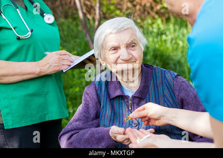 Personnes âgées femme malade recevant les pilules d'une infirmière, médecin écrit prescription médicale dans l'arrière-plan Banque D'Images