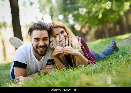 Beau jeune couple portant sur l'herbe dans un parc urbain. Homme de race blanche et femme portant des vêtements décontractés. Femme blonde. Banque D'Images