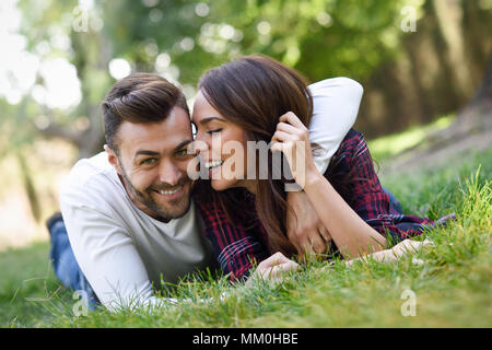 Beau jeune couple portant sur l'herbe dans un parc urbain. Homme de race blanche et femme portant des vêtements décontractés. Banque D'Images