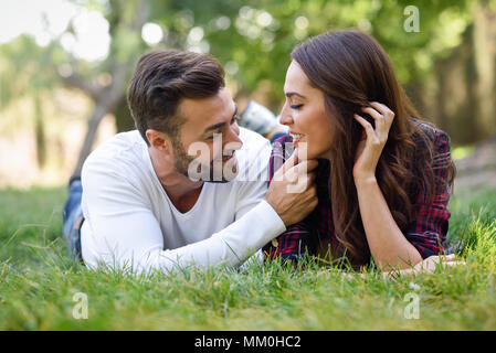 Beau jeune couple portant sur l'herbe dans un parc urbain. Homme de race blanche et femme portant des vêtements décontractés. Banque D'Images