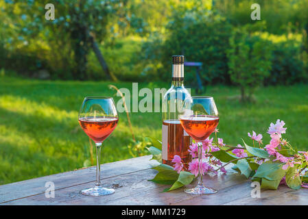 Une bouteille et deux verres de vin rose sur la vieille table en bois dans le jardin en fleurs Banque D'Images