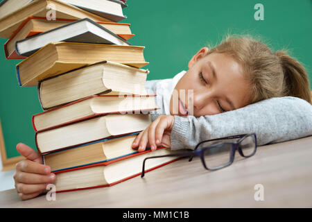 Fille de l'école fatigué s'est endormi sur la table entre les livres. Photo de petite fille à l'école. Concept de l'éducation Banque D'Images
