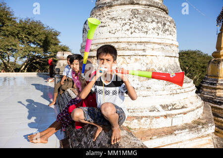 Bagan, Myanmar, 29 Décembre 2017 : Groupe d'enfants sont assis en face d'un stupa et faire du bruit avec les vuvuzelas à Bagan, Myanmar Banque D'Images