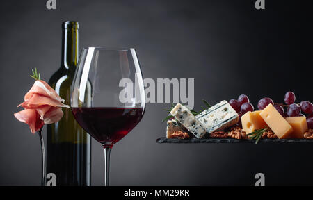 Verre de vin rouge avec différents fromages, fruits et jambon sur un fond noir. L'espace de copie . Banque D'Images