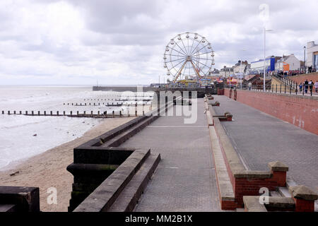 Bridlington, Yorkshire, UK. Le 29 avril 2018. Les vacanciers à la promenade et la fête foraine grande roue découpé sur un ciel nuageux . Banque D'Images