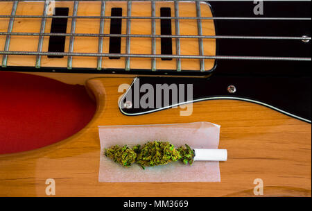 Joint de marijuana prêt à rouler sur une basse électrique vintage de quatre cordes. Instrument de musique et les drogues, concept de rechercher l'inspiration. Banque D'Images