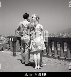 Années 1960, historcial, deux touristes debout à l'extérieur à la recherche sur la ville de Rome, Italie. L'homme est à l'écoute des informations touristiques à partir d'un téléphone, tandis que la femme porte une robe motif floral de l'époque. Banque D'Images