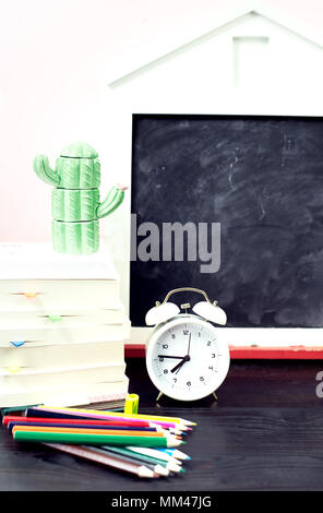 Les fournitures scolaires réveil sur table. Concept Retour à l'école avec tableau noir craie, crayons, livres, cactus figure Banque D'Images