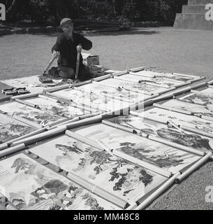 Années 1960, historiques, homme artiste japonais avec son dessin affiché sur l'herbe à l'extérieur. Ces sont traditionnels kakemono ou kakejiku, faites défiler et peintures sont conçus pour accrochées sur un mur. Banque D'Images