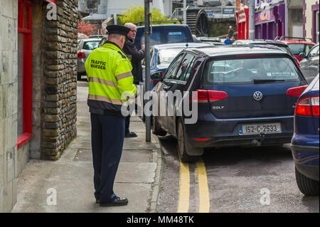 Trafic irlandais Préfet émet un ticket de parking pour une voiture qui est garé sur double lignes jaunes et le trottoir à Bantry, dans le comté de Cork, Irlande. Banque D'Images