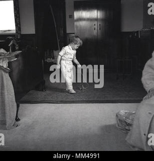 Années 1960, historique, un jeune garçon en pyjama tire son nouveau jouet avion le long du plancher de chambre à coucher de ses parents, juste après avoir reçu comme cadeau d'anniversaire, England, UK. Banque D'Images