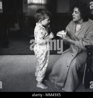 Années 1960, historiques, jeune garçon dans son pyjama mettre le récepteur d'un téléphone jouet étant détenu par sa mère à l'oreille, ayant été donné comme un cadeau d'anniversaire, England, UK. Banque D'Images