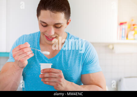 Jeune homme de manger du yogourt dans la cuisine prendre un petit déjeuner sain smiling Banque D'Images