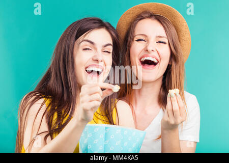 Deux jolies filles souriant s'amusant à regarder film avec pack de popcorn sur fond bleu Banque D'Images