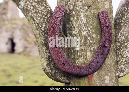 Rusty metal lucky horseshoe cloué à un poteau en bois avec de vieux bâtiment en ruine en arrière-plan Banque D'Images