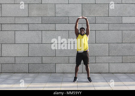 Coureur de l'homme sportswear jaune avant de faire l'étirement exercices du matin. Jeune africain jogger en préchauffage avant d'exécuter en plein air Banque D'Images