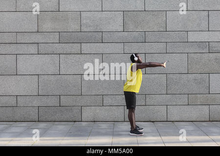 En homme sportswear jaune avant de faire l'étirement exercices du matin. Jeune africain jogger en préchauffage avant d'exécuter en plein air Banque D'Images