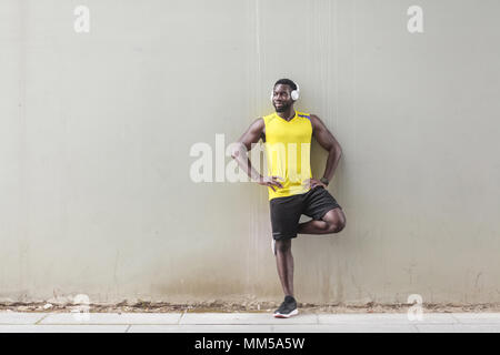 Afro sportive homme debout près de l'ancien mur, faisant gymnastique matinale. Tourné en extérieur, le matin. Printemps ou été Banque D'Images
