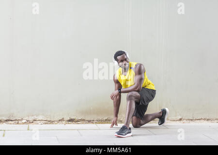 Coureur en jaune d'Afrique s'étendant de vêtements avant de faire exercices du matin à la caméra en souriant à pleines dents nd. Tourné en extérieur, le matin. Printemps ou summ Banque D'Images