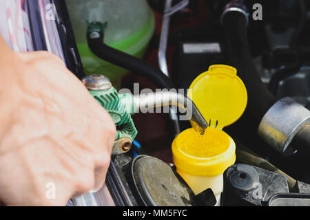 Libre d'un jeune homme de race blanche de remplir le réservoir de liquide lave-glace d'une voiture avec de l'eau d'un tuyau Banque D'Images