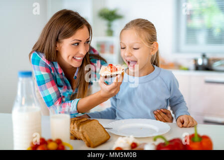 La mère est l'alimentation de sa fille avec le sandwich ils ont juste pris dans la cuisine domestique. Banque D'Images