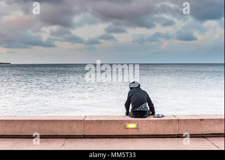 Un jeune homme solitaire seul site sur la plage à pied face à la mer à Cairns, en Australie. Banque D'Images