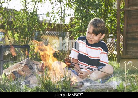 Les enfants bénéficient de camp. Boy toasting saucisses sur le jardin. Banque D'Images