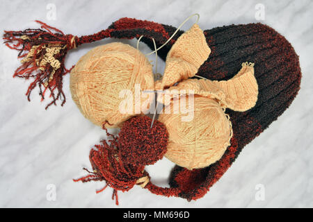 Le tricot de laine au moyen de rayons.produit fini-children's hat et une boule de fils de laine sur fond gris Banque D'Images