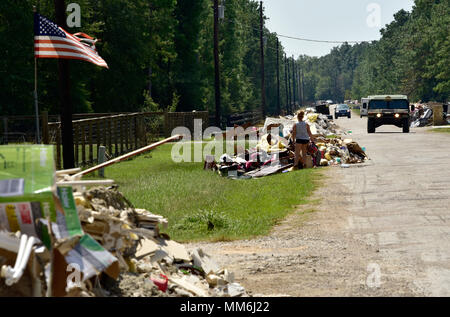 Ancienne gloire des mouches, un Texan examine les débris, et d'une garde nationale de l'Arkansas Multi très mobile véhicule à roues (HMMWV) patrouille dans les rues de Lumberton, Texas le 11 septembre suite à l'ouragan Harvey. Soldats assigné à la force de l'équipe d'évaluation des dommages des Aléoutiennes, une composante de la Force opérationnelle de l'Arkansas, est sorti dans la communauté de Lumberton inondées récemment, pour signaler les dommages estimés pour chaque chambre, dans leur zone d'opérations, pour le haut commandement. Cette photo sert seulement comme un petit instantané de l'ensemble de la dévastation aux régions touchées par l'ouragan Harvey. Banque D'Images