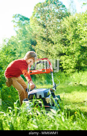 Garçon enfant aider dans le jardin la pelouse avec une tondeuse Banque D'Images