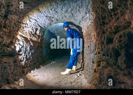 Dans l'homme dark old tunnel. Bastion passage sous le tunnel d'escaliers de la ville avec des murs faits de pierre de sable orange. Le personnel dans l'ensemble bleu et casque de sécurité Banque D'Images