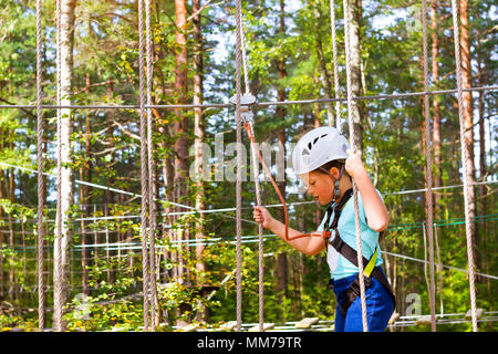 Adolescente poursuit en sentier à charnière dans l'extrême parc en forêt de l'été. L'escalade de haute altitude de la formation sur l'enfant parcours aventure, équipé de sa Banque D'Images