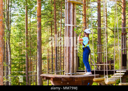 Adolescente poursuit en sentier à charnière dans l'extrême parc en forêt de l'été. L'escalade de haute altitude de la formation sur l'enfant parcours aventure, équipé de sa Banque D'Images