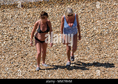 Deux femmes âgées vieillissement marche sur une plage de galets sur une chaude journée d'été portant des maillots de bain. les retraités en maillot de marcher sur des cailloux. Banque D'Images