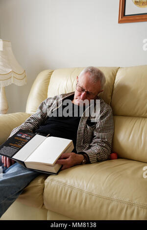 Homme Anolder sont endormis sur le canapé tout en lisant un livre Banque D'Images