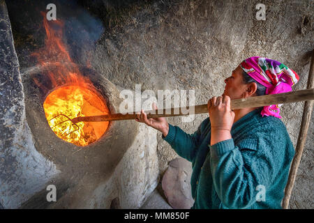 Boukhara, Ouzbékistan - 20 Avril 2018 : une femme âgée allumant un tandoor - un traditionnel four ouzbek utilisées dans la cuisine et la cuisson du pain plat Banque D'Images