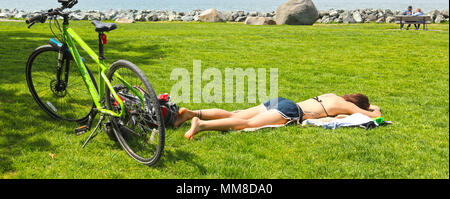 Jeune femme pose dans l'herbe au Boulevard Park pendant que son soleil vélo est derrière elle. Un vieux couple est assis sur un banc de parc en backgrund Banque D'Images