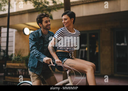 Heureux jeune homme monte un vélo avec femme assise sur le guidon. Couple romantique balade à vélo dans la ville. Banque D'Images