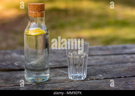 Une bouteille d'eau avec du citron et un verre. Un banc sur lequel est placée une boisson rafraîchissante. La saison de printemps. Banque D'Images