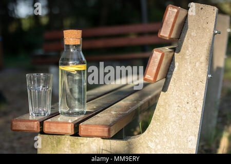 Une bouteille d'eau avec du citron et un verre. Un banc sur lequel est placée une boisson rafraîchissante. La saison de printemps. Banque D'Images