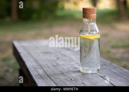 Une bouteille d'eau avec du citron et un verre. Un banc sur lequel est placée une boisson rafraîchissante. La saison de printemps. Banque D'Images