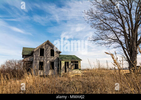 Une vieille ferme abandonnée effrayante maison qui est de se détériorer avec le temps avec un vieil arbre et couronné par un magnifique ciel partiellement nuageux. Banque D'Images