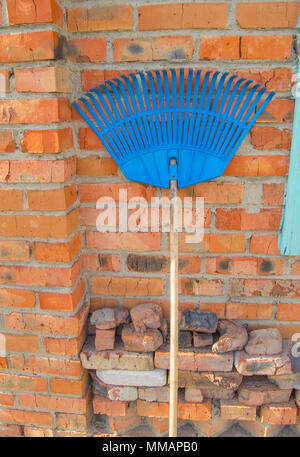 Râteau en plastique bleu pour la récolte les feuilles et le gazon sont près de la red brick wall Banque D'Images