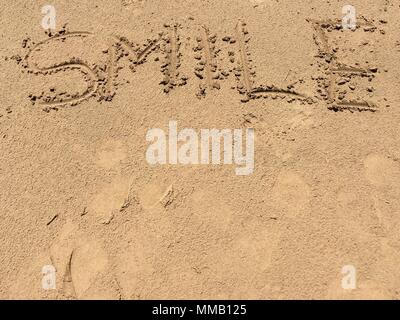 Le mot sourire écrit dans le sable sur une plage marocaine comme un message heureux Banque D'Images