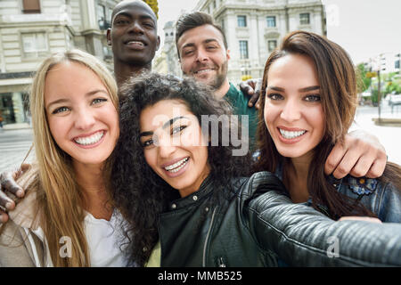 Groupe multiracial d'amis prenant en selfies une rue urbaine avec une femme musulmane en premier plan. Trois jeunes femmes et deux hommes portant des vêtements décontractés. Banque D'Images