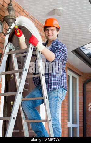 Portrait of smiling handyman grimper sur l'escabeau pour réparer un lampadaire Banque D'Images