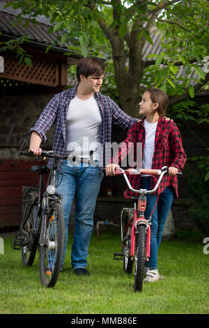 Jeune homme avec teenage Girl standing avec des vélos à chambre jardin Banque D'Images