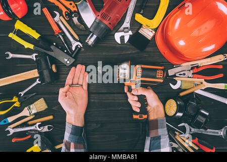 Cropped shot of worker holding tournevis électrique et diverses fournitures de bureau en bois Banque D'Images