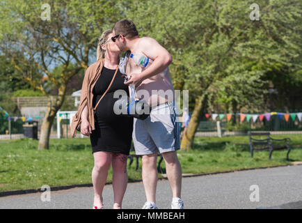 Un jeune couple s'embrasser dans un parc sur une chaude journée de l'UK. L'affichage public d'affection. PDA. Banque D'Images