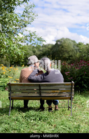 Mari et femme, vue arrière d'un homme âgé portant un chapeau et femme assise côte à côte sur un banc dans un jardin. Banque D'Images